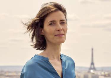 Anne-laure pressat smiling in paris wearing blue blouse.