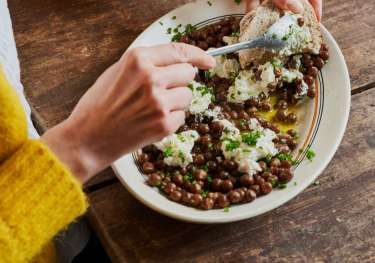 Woman eating bean dish with hunk of bread.