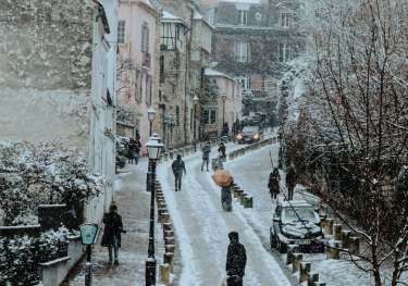 People walking down road in parisian neighbourhood during winter with snow.